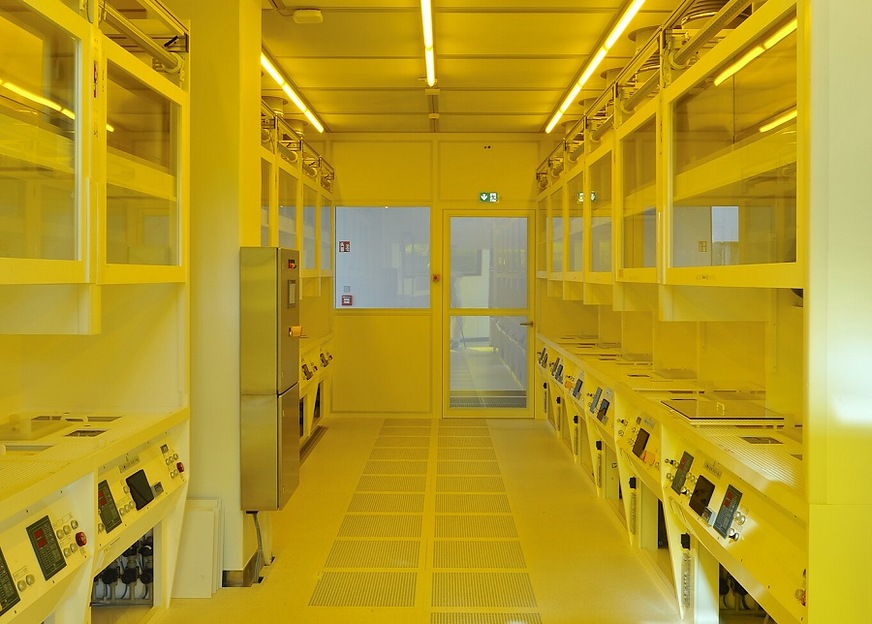 View into the corridor of the clean room. In the back one can see the yellow light from the photolithography laboratory.