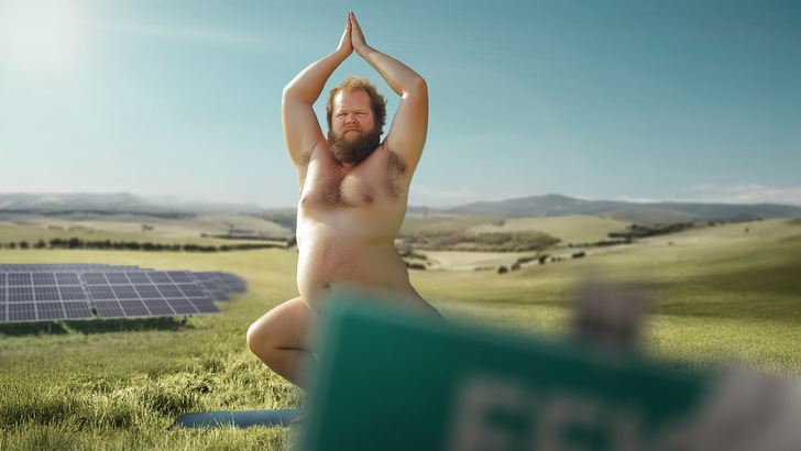 Ein nackter Mann macht Yoga im Freien in der Nähe von Solarmodulen auf einer Wiese mit Hügeln im Hintergrund. - © PMT 2025