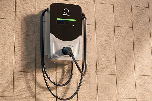 Wall-mounted electric vehicle charger with a connected charging cable on a beige tiled wall. - © Sonnen