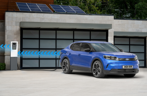 Blue electric SUV charging at a station in front of a modern, solar-paneled garage. - © Ford
