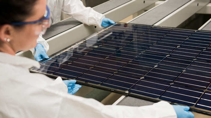 Two workers in protective gear and gloves carefully handling a large solar panel in a lab. - © Oxford PV